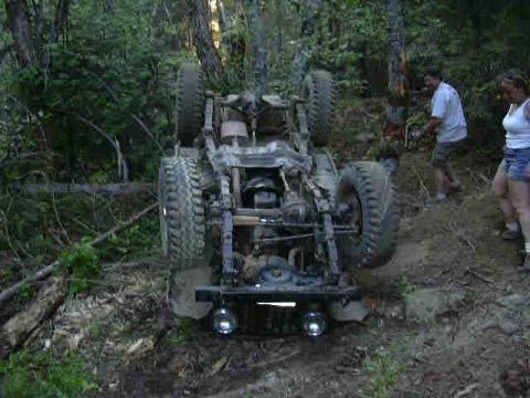 1988 Ford Bronco - An off-road vehicle has overturned on a wooded trail, with two onlookers observing the scene.