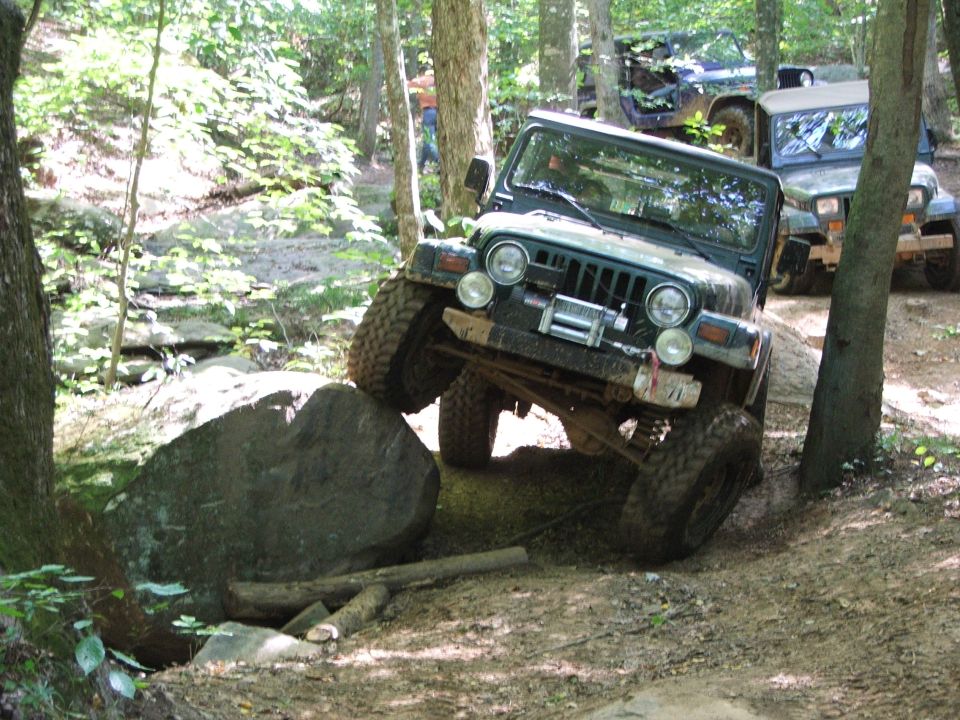 Jeep Wrangler navigating a rocky trail, with other Jeeps behind it
