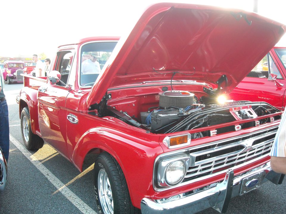Red pickup truck with hood open, showing engine. Ford badging visible