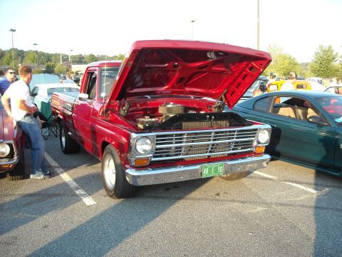 1979 Ford F-150 - A red pickup truck is parked at a car show with its hood open, revealing the engine. Another car is visible to the right.