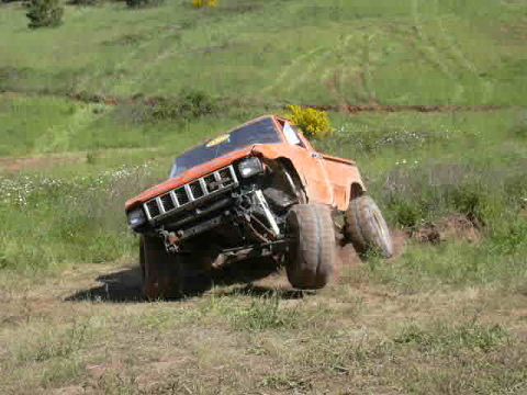 1988 Ford Bronco - An orange off-road vehicle navigates a grassy incline with its wheels turned.