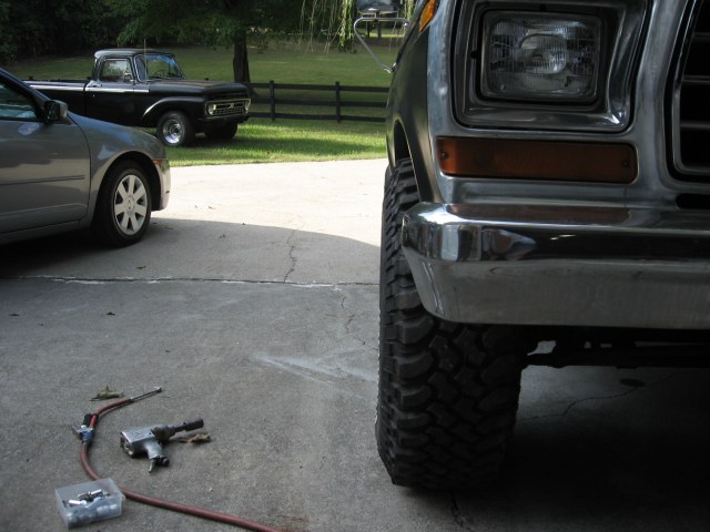 Front corner of a Ford truck on mud tires with an air impact wrench and lug nuts on the driveway