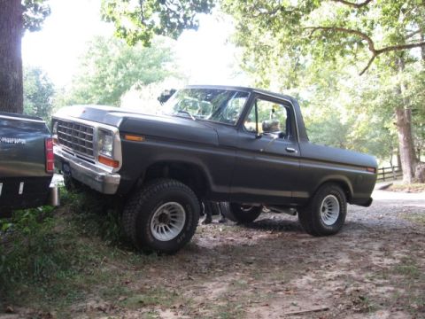 1978 Ford Bronco - This dark 1978 Ford Bronco is parked on a dirt incline, partially obscured by another vehicle.
