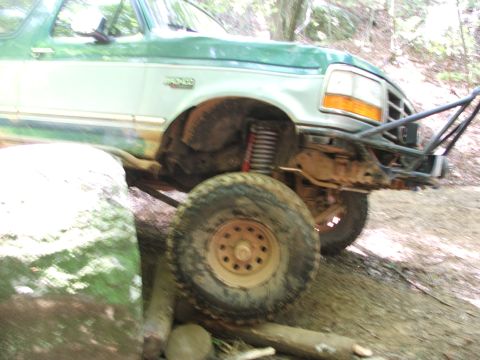 1996 Ford Bronco - A green Ford Bronco navigates a challenging off-road trail, with one wheel elevated on a rock.