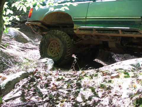 1996 Ford Bronco - This green SUV navigates a challenging off-road trail, its suspension and tires.