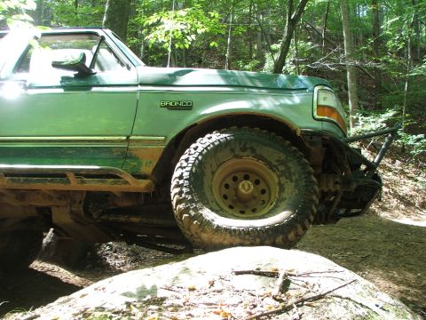 1996 Ford Bronco - Green 1996 Ford Bronco navigating a rough, wooded trail with large tires.