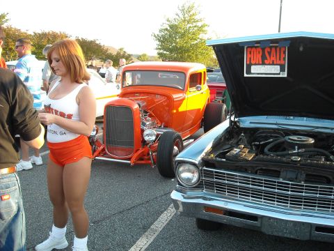 1979 Ford F-150 - Two cars are parked at an outdoor event, one a bright orange hot rod and the other a silver classic with its hood up.