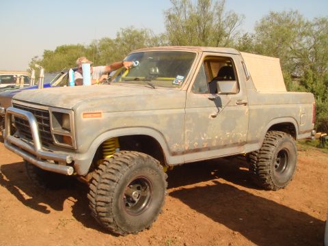 1992 Ford Bronco - A person cleans the windshield of a lifted, off-road SUV with a light-colored camper shell.