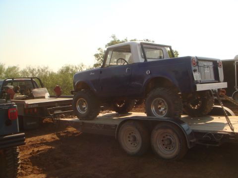 1992 Ford Bronco - A blue International Scout II is loaded onto a trailer, with another truck visible on a separate trailer behind it.