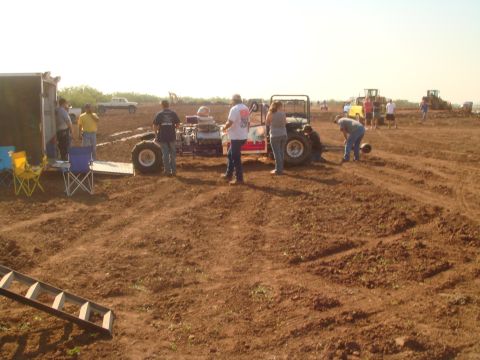 1992 Ford Bronco - People and vehicles at a mud bog racing event with a trailer and construction equipment visible.