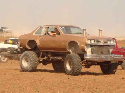 1992 Ford Bronco - A heavily modified coupe with oversized tires and dual exhaust stacks sits on a trailer in a dirt lot.