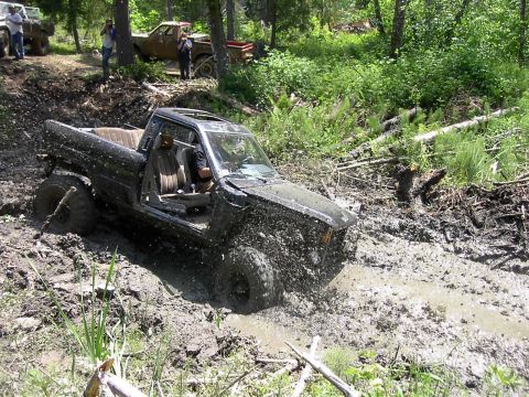 1988 Ford Bronco - A black pickup truck is stuck in deep mud off-road, with other vehicles visible in the background.