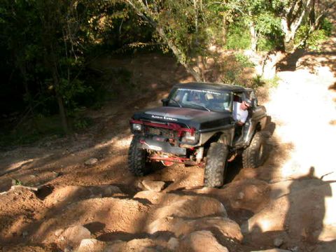 1990 Ford Bronco - A black Ford Bronco navigates a rocky off-road trail with trees in the background.