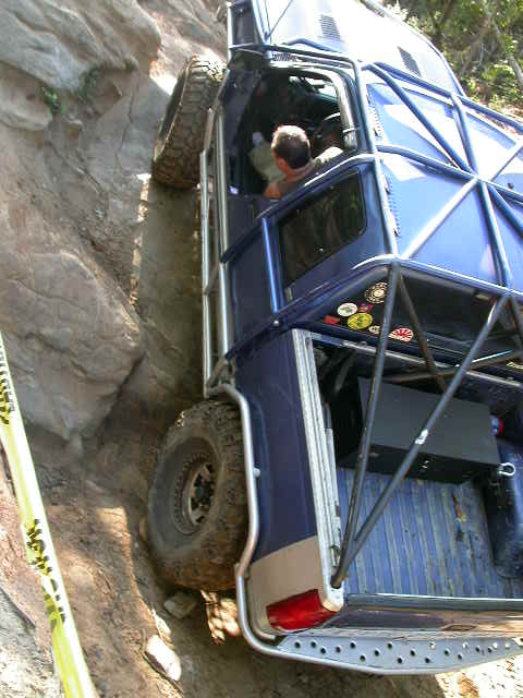 1990 Ford Bronco - This heavily modified off-road vehicle navigates a challenging rocky terrain, with its tires gripping the steep incline.