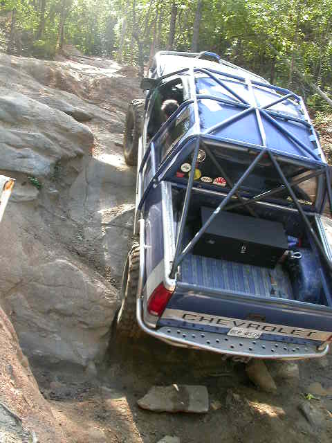 1990 Ford Bronco - A blue Chevrolet truck navigates a challenging rocky incline on an off-road trail.