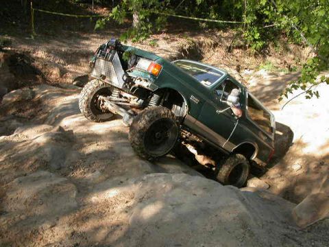 1990 Ford Bronco - 1990 Ford Bronco navigating a challenging off-road course with large tires and lifted suspension.