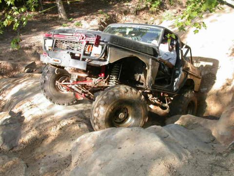 1990 Ford Bronco - A modified black Ford Bronco tackles a challenging off-road course with large tires and a custom front end.