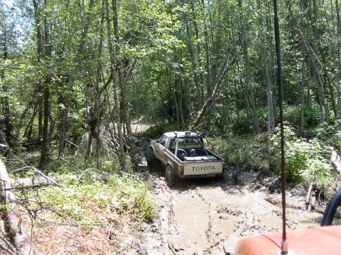 1988 Ford Bronco - Toyota pickup truck driving through mud on a forest trail. Another vehicle is in the foreground.