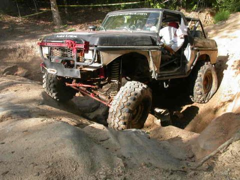 1990 Ford Bronco - This heavily modified truck is shown tackling a challenging off-road course with large rocks and dirt mounds.