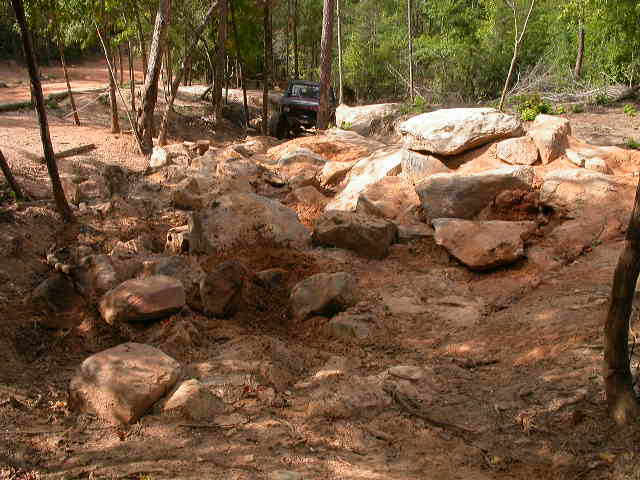 Dark off-road vehicle navigating a rocky, wooded trail