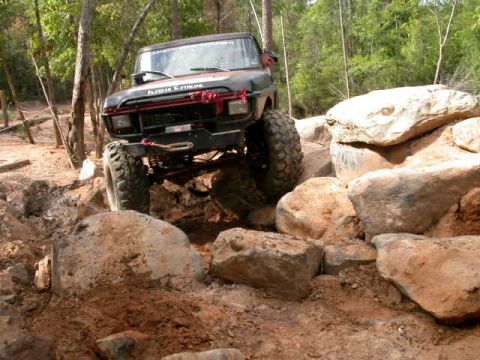 1990 Ford Bronco - Off-road Bronco tackling a difficult rock obstacle on a wooded trail.