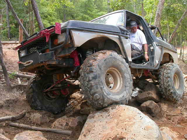 Off-road vehicle with large tires navigating rocky terrain. Driver is visible inside