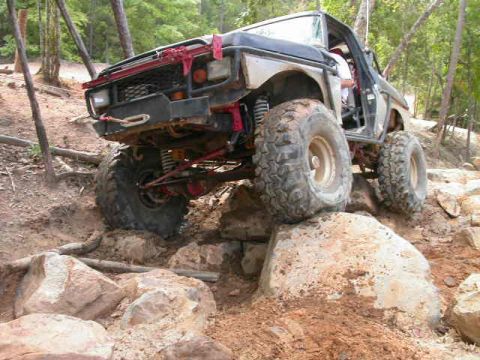1990 Ford Bronco - This modified Ford Bronco navigates a challenging rocky terrain on a wooded trail.