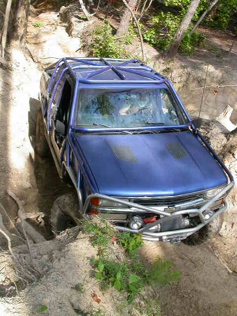1990 Ford Bronco - This blue SUV is navigating a challenging off-road trail with steep inclines and rough terrain.