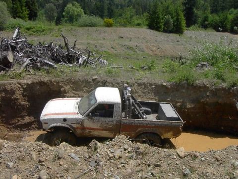 1988 Ford Bronco - This pickup truck is stuck in a muddy pit with trees and debris in the background.