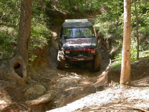 1990 Ford Bronco - Vehicle is on a challenging off-road trail, with mud covering the tires and the path.