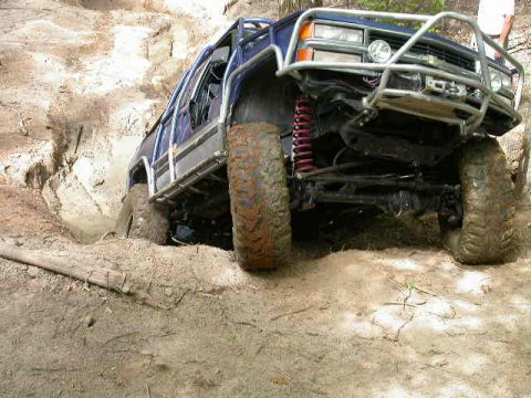 1990 Ford Bronco - Modified SUV tackles a challenging off-road obstacle on a dirt track.
