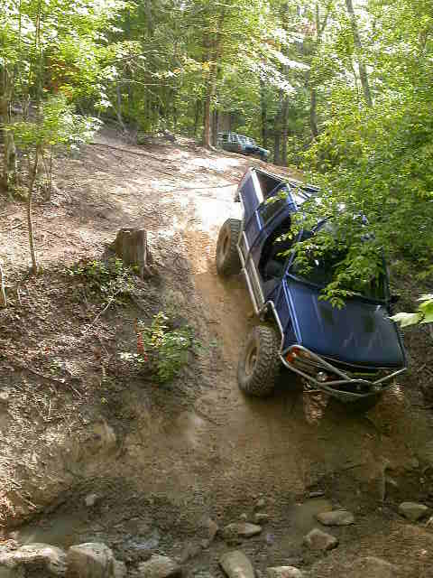 1990 Ford Bronco - Off-road vehicles tackle a challenging muddy incline in a forest setting.