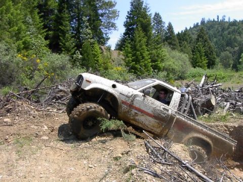 1988 Ford Bronco - A white pickup truck navigates a challenging off-road terrain, getting stuck in a ditch.