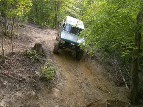 1990 Ford Bronco - A green SUV navigates a challenging dirt trail through a wooded area.