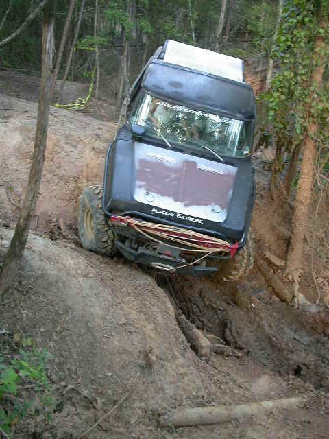 1990 Ford Bronco - A black Ford Bronco navigates a steep, muddy incline in a wooded area.
