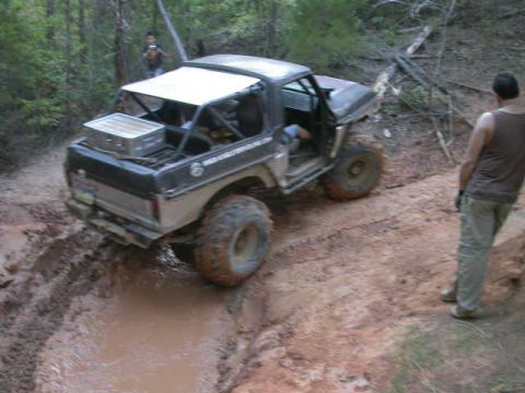 1990 Ford Bronco - This Ford Bronco navigates a challenging muddy trail, with a spectator observing the off-road action.
