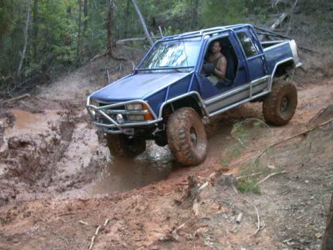 1990 Ford Bronco - A blue pickup truck navigates a muddy trail in a wooded area.