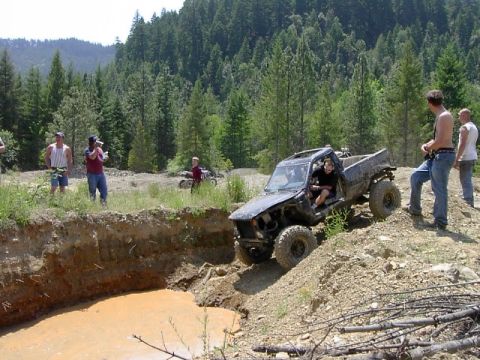 1988 Ford Bronco - A group of people watch as a modified pickup truck navigates a challenging off-road course with a muddy water hazard.