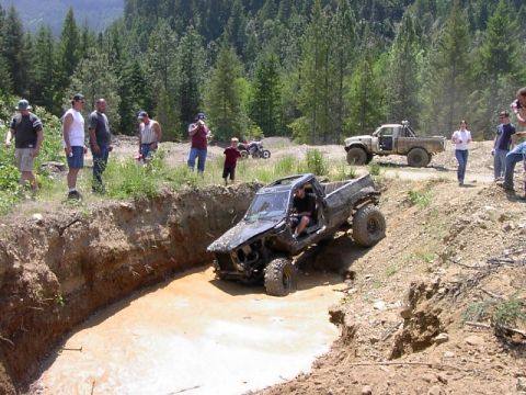 1988 Ford Bronco - Several people watch as a heavily modified pickup truck navigates a challenging off-road course.