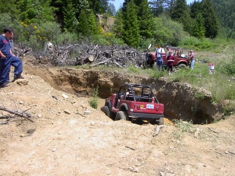 1988 Ford Bronco - A red off-road vehicle navigates a challenging dirt trench during an off-road event.