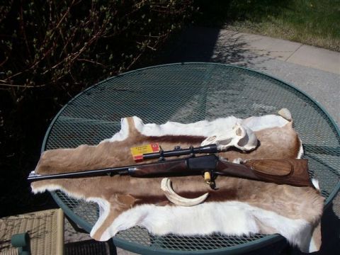 1991 Ford Bronco - A hunting rifle, ammunition, and animal skull are displayed on a fur pelt atop a metal table outdoors.