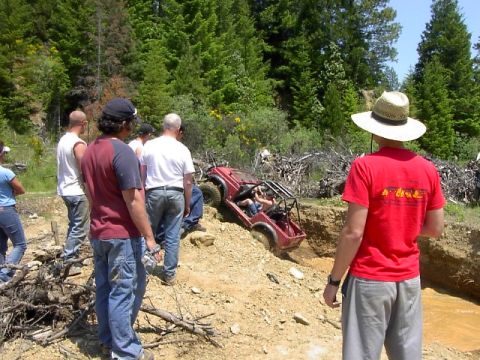 1988 Ford Bronco - Off-road buggy stuck in a mud pit with several people watching.