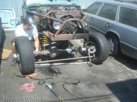 1987 Suzuki Samurai - Mechanic works on the front suspension and engine of a 1987 Suzuki Samurai, which has a custom roll cage.