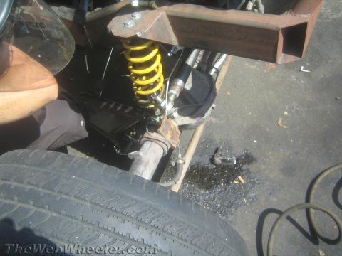 1987 Suzuki Samurai - A mechanic works on the suspension system of a vehicle, with a tire and frame components visible.