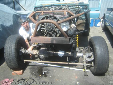 1987 Suzuki Samurai - A mechanic works on the front end of a modified 1987 Suzuki Samurai, revealing its engine and custom roll cage.