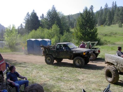1988 Ford Bronco - Several off-road vehicles are gathered in a grassy, wooded area with portable toilets in the background.