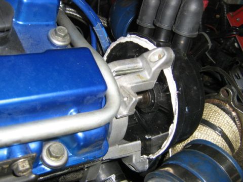 1995 Ford Probe - Tight engine-bay shot of a blue-painted valve cover next to a cut-open black rubber boot revealing a cast aluminum bracket and a shaft with…