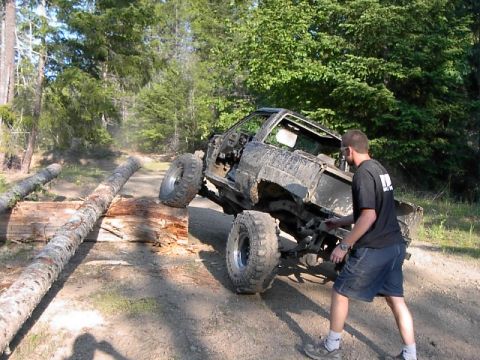 1988 Ford Bronco - A heavily modified off-road truck attempts to climb over a series of logs on a dirt path, with a person observing the action.