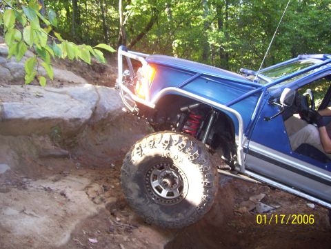 1978 Ford Bronco - This modified off-road vehicle navigates a challenging rocky incline on a wooded trail.