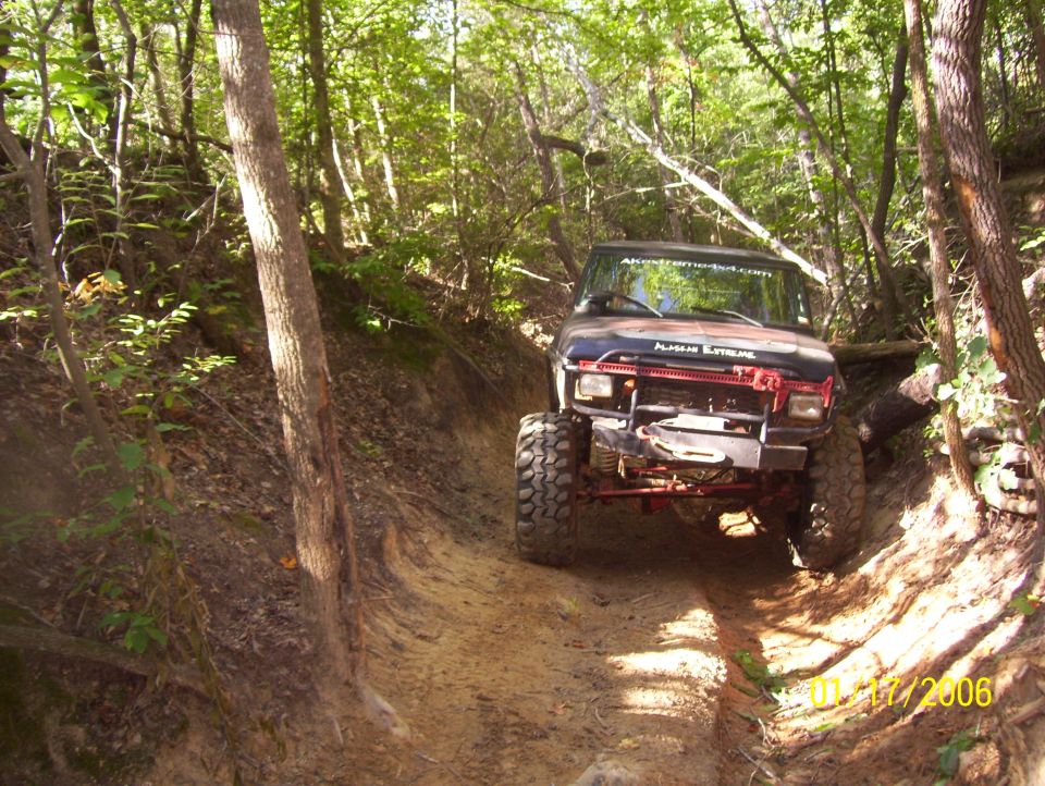 Off-road vehicle with large tires navigating a steep dirt trail in a wooded area